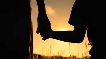 Silhouette of mother and child holding hands facing the sunset.