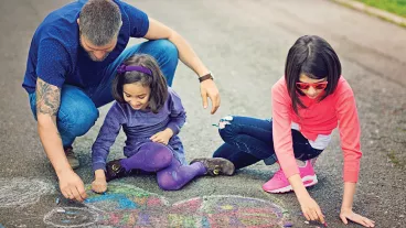 Father and his daughters are drawing butterfly with chalk.