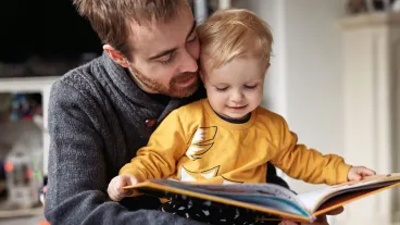 Cropped shot of an adorable smiling little boy reading a book while sitting with his father at home
