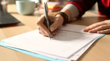 Close up of student girl hand filling out form on a desk at home at night