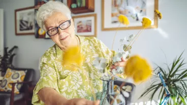 Senior woman arranging flowers in a vase at home.