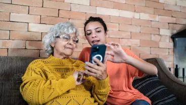 Granddaughter helping grandmother to use the mobile phone at home.