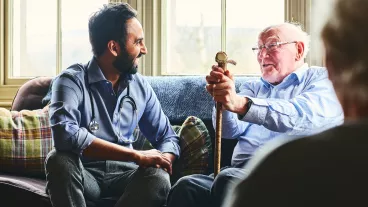 Young male doctor and senior man sitting on sofa and smiling during home visit.
