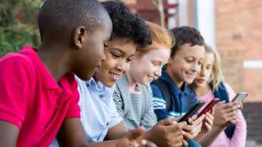 Group of multiethnic children sitting in a row and typing messages on their smartphones.
