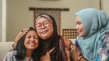 A portrait of happy Asian Muslim young girl with mother and grandmother sitting at home during Hari Raya celebration