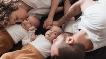 Happy young family with newborn twin babies lying on the bed together, parents holding hands and kissing their babies Happy young family with newborn twin babies lying on the bed together, parents holding hands and kissing their babies