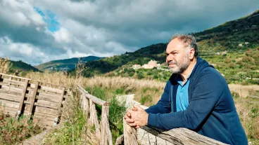 Side view of a happy thoughtful bearded mature man contemplating mountain nature with cloudy sky near wooden footbridge. Concept of leisure activities,tourism, lifestyle e nature