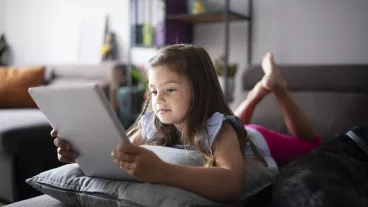 little girl laying on sofa at home and using digital tablet.