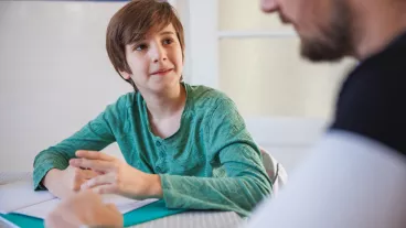 Elementary aged boy doing homework at the dining table and looking at his father