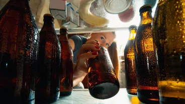 Caucasian woman takes cold refreshing beer from out the fridge, inside view from fridge of hand holding the bottle. Alcohole, domestic life, entertainment, drink concept. Cold cola or beer bottles.