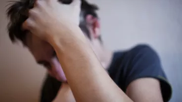 A teenager in a state of shock and depression squeezes his head with his hands on a light background