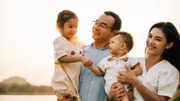 Portrait of happy family enjoying a beautiful spring day in park, with their cute baby and lovely nature surrounding them outdoor.