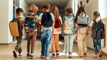A group of schoolchildren with backpacks walk along the school corridor during recess.