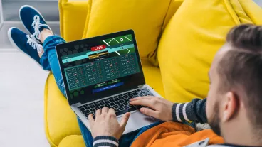 Cropped shot of a man lying on sofa making bets online at bookmaker's website using laptop.