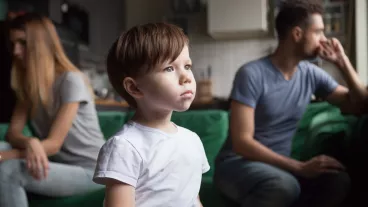 Upset frustrated little boy tired of parents fight, toddler son looking out window reaming that family conflicts would stop while parents sitting separately on sofa, suffering from mom and dad quarrel