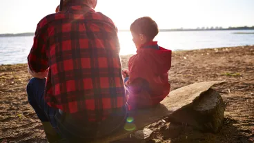 Fisherman and his grandson sitting on riverbank at sunset