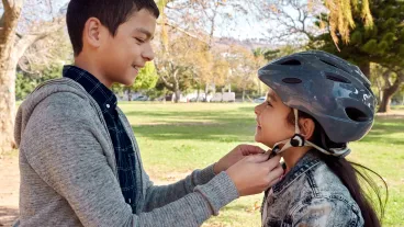 Shot of a young boy helping to secure his sister’s helmet before she rides her bicycle in the park Shot of a young boy helping to secure his sister’s helmet before she rides her bicycle in the park