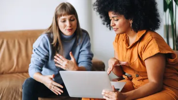 Two young businesswomen having a discussion while looking at a laptop screen. Two female entrepreneurs working as a team in a modern workplace.