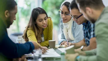 A multi-ethnic group of business people are indoors in an office boardroom. They are sitting around a table and making plans. A multi-ethnic group of business people are indoors in an office boardroom. They are sitting around a table and making plans.