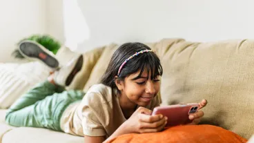 Young girl watching video (or playing mobile games) on mobile phone at home