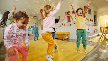 Group of happy children having fun playing with soap bubbles in a playroom.