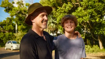 Father and teenage son smiling and embracing in a moment of affection.