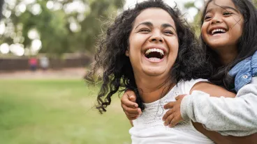 Happy mother giving her child a piggyback ride outdoors in a grassy park setting..