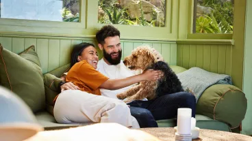 Laughing young couple petting their dog while sitting together on a sofa in their living room at home