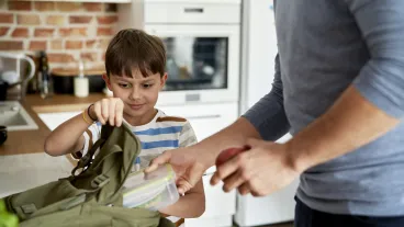 Father packing healthy food lunch boxes for son.