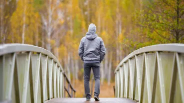 One young man in gray clothes slowly walking on bridge at natural park in colorful autumn day.