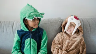 Two boys in animal costumes sitting together on a sofa indoors.
