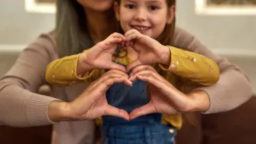 Closeup view unrecognised woman and young girl showing heart signs with their hands.