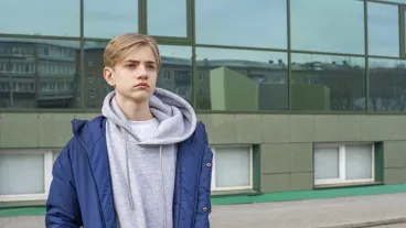 Boy teenager in a jacket and a hoodie stands against the background of the college building.