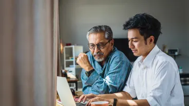 Asian senior father and his adult son using laptop computer while sitting at home