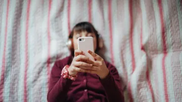 A teenager lying in bed looking at her phone.