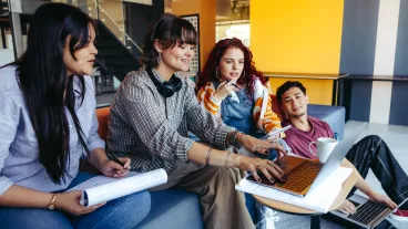 A casual group of young adults engages in a collaborative project using laptops in a contemporary office, emphasizing teamwork and creativity.