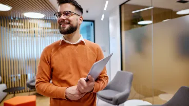 Young businessman holding a tablet and smiling in a modern office, looking away with a sense of confidence and ambition, embodying the spirit of innovation and success