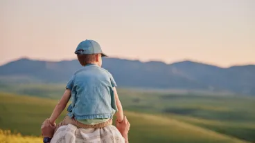 Shoulder carry, back and boy with father in field for bonding, travel and adventure on vacation. Outdoor sunset, space and boy with dad for view in nature together for holiday, love and weekend trip