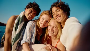 Young man holding phone and taking photo of himself with three friends