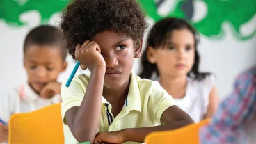 A photo of a young boy in a classroom and behind him are two young children blurred out in the background