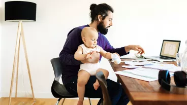 Young father working from home on his laptop with his baby in his lap