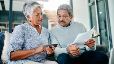 Shot of a mature couple using a mobile phone while going through paperwork together at home