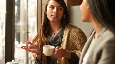 Cropped shot of an affectionate young gender fluid person having a discussion with their friend while having coffee in a cafe