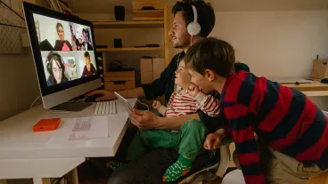 Photo of a man working from home, with his sons keeping him company, having a video conference call