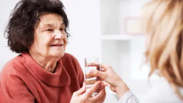 Home nurse helping a senior woman at home. She is giving a glass of water to her.