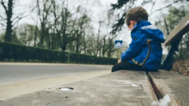 Sad boy in a blue jacket sitting alone on a wooden bench