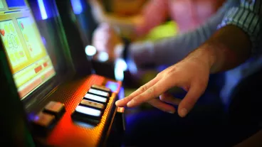 Closeup of unrecognizable man making money on slot machine in casino. He's playing slot poker. There are blurry people in background also playing.