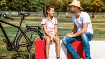 Smiling father sitting with teenage daughter in park