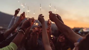 Group of friends holding burning sparklers against the sky