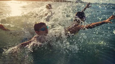 Brothers and sister are having fun in sea waves. Kids are jumping into incoming waves and laughing on a Sunny summer day evening. 